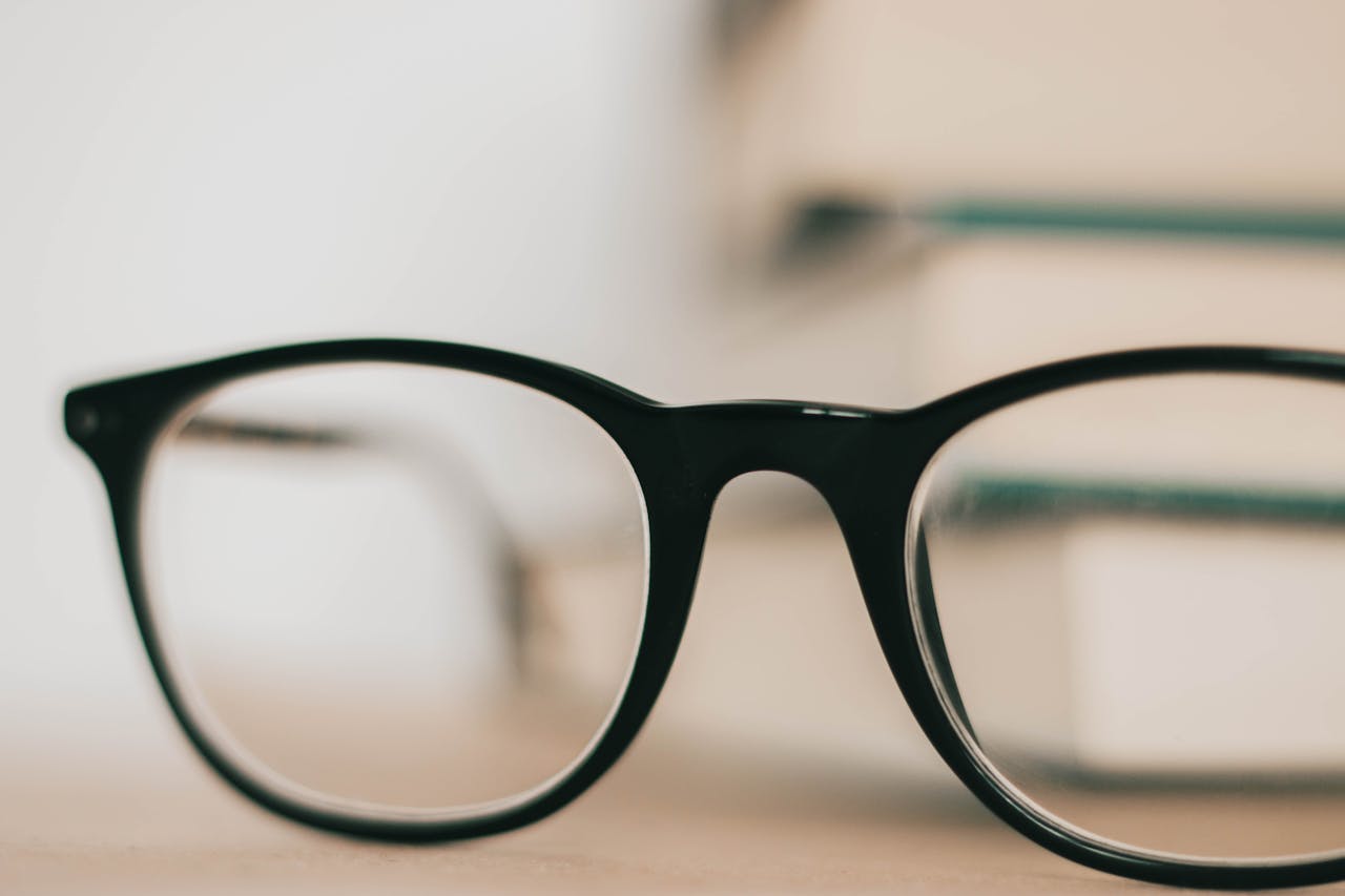 Stylish black-rimmed eyeglasses on a blurred bookshelf background for modern design.
