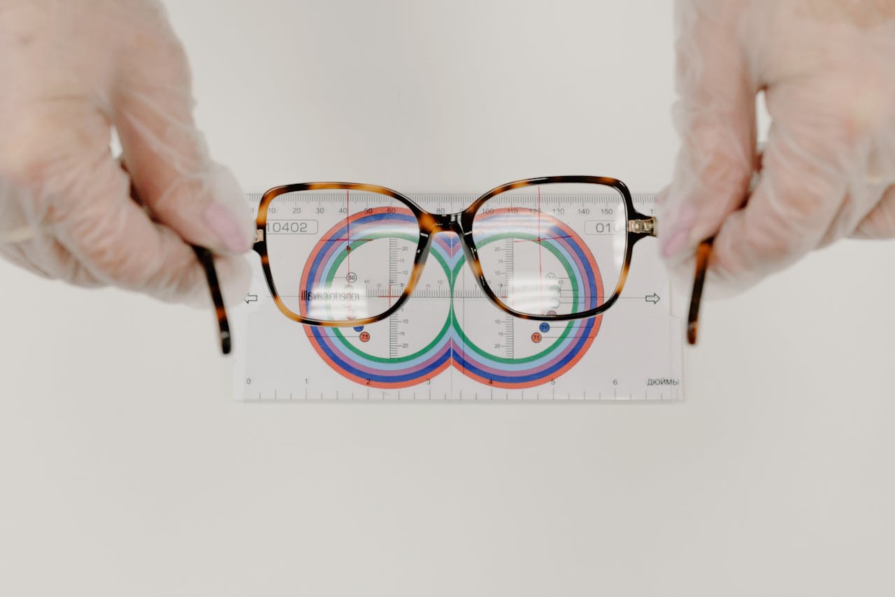 From above of crop anonymous oculist in sterile gloves measuring modern eyewear with optical tool on white background