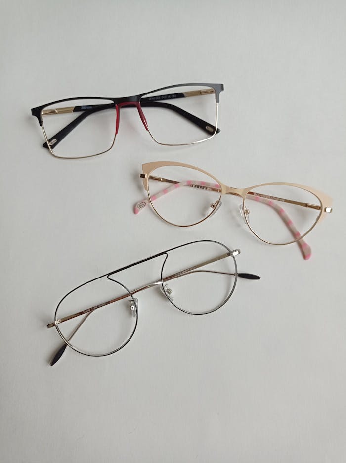 A flat lay of three stylish eyeglasses on a white surface, showcasing fashion eyewear trends.